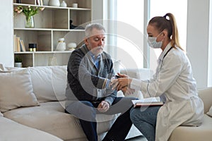 Female doctor senior man taking his blood pressure in doctor office or at home. Old man patient and doctor have