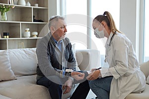 Female doctor senior man taking his blood pressure in doctor office or at home. Old man patient and doctor have