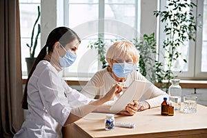 Female doctor and senior woman, patient wearing face mask, having appointment in office. Checkup and treatment after