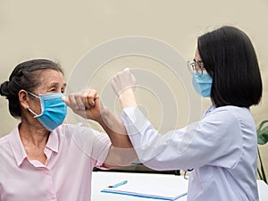 Female Doctor and senior woman waring protective medical mask, use arm tagging each other in a clinic after doctor visiting,