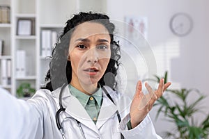 Female doctor is serious, looking worriedly into smartphone camera talking to patient remotely, reporting disappointing