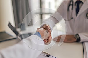 Female doctor shaking hands with patient while sitting at desk in clinic. Focus on the hands - handshake