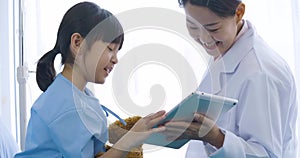 Female doctor showing digital tablet computer and talking with young patient girl with happy emotion