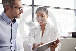 Female Doctor Showing Mature Male Patient Test Results On Digital Tablet In Office