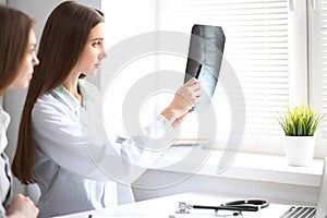 Female doctor showing x-ray to her patient while sitting at the table near the window in hospital. Physician is ready to