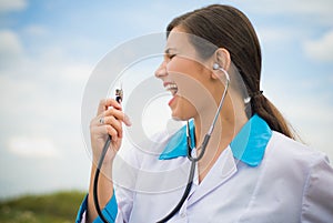 Female doctor singing in stethoscope over blue sky