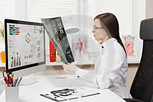 Female doctor sitting at desk with computer, film x-ray the brain by radiographic image ct scan mri in light office in