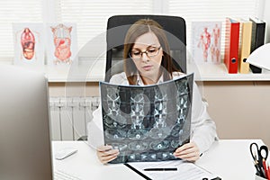 Female doctor sitting at desk with computer, film x-ray the brain by radiographic image ct scan mri in light office in