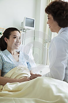 Female doctor sitting on hospital bed and discussing with young female patient