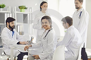Female doctor sitting at a table with collegues in white lab coats at a medical hospital.