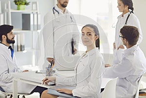 Female doctor sitting at a table with collegues in white lab coats at a medical hospital.