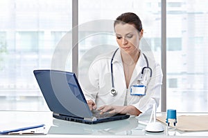 Female doctor sitting at table with laptop