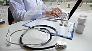 A female doctor sitting at work examines the patient`s history and uses a laptop to record patient information at the hospital.