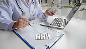 A female doctor sitting at work examines the patient`s history and uses a laptop to record patient information at the hospital.