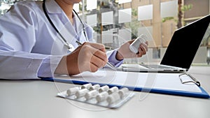 A female doctor sitting at work examines the patient`s history and uses a laptop to record patient information at the hospital.