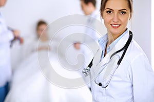 Female doctor smiling on the background with patient in the bed and two doctors