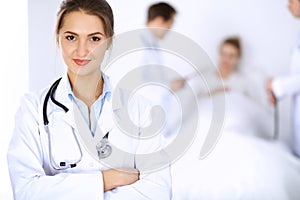 Female doctor smiling on the background with patient in the bed and two doctors