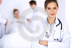 Female doctor smiling on the background with patient in the bed and two doctors