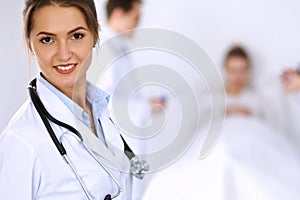 Female doctor smiling on the background with patient in the bed and two doctors