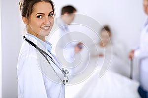 Female doctor smiling on the background with patient in the bed and two doctors