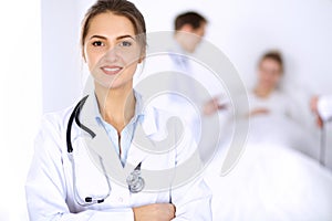 Female doctor smiling on the background with patient in the bed and two doctors