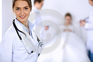 Female doctor smiling on the background with patient in the bed and two doctors