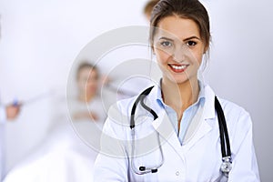 Female doctor smiling on the background with patient in the bed and two doctors