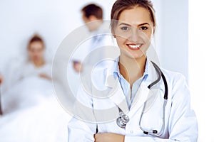 Female doctor smiling on the background with patient in the bed and two doctors