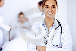 Female doctor smiling on the background with patient in the bed and two doctors