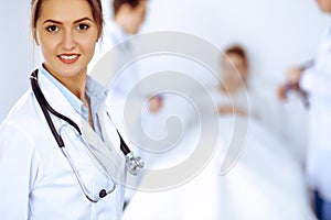 Female doctor smiling on the background with patient in the bed and two doctors