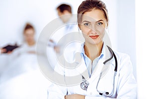 Female doctor smiling on the background with patient in the bed and two doctors
