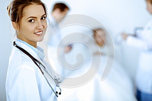 Female doctor smiling on the background with patient in the bed and two doctors