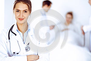 Female doctor smiling on the background with patient in the bed and two doctors