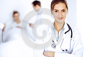 Female doctor smiling on the background with patient in the bed and two doctors