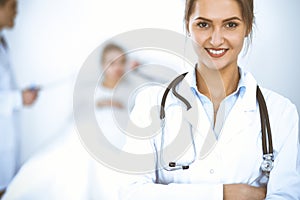 Female doctor smiling on the background with patient in the bed and two doctors