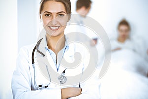 Female doctor smiling on the background with patient in the bed and two doctors