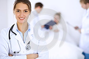 Female doctor smiling on the background with patient in the bed and two doctors