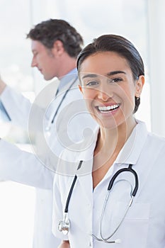 Female doctor smiling at camera while her colleague looking at X-ray