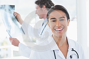 Female doctor smiling at camera while her colleague looking at X-ray