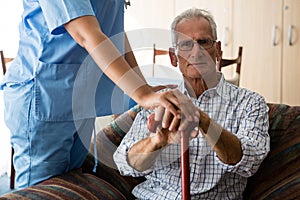 Female doctor standing by senior man sititng on sofa in nursing home