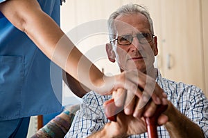 Female doctor standing by senior man sititng on sofa in retirement home