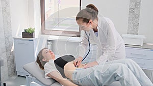 A female doctor with a stethoscope examines the abdomen of a young patient lying on a bed in the emergency department of