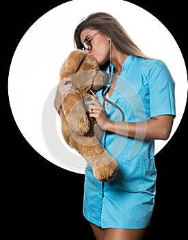 female doctor with stethoscope heals a teddy bear on a white circle and black background