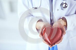 Female doctor with stethoscope holding heart, on light background