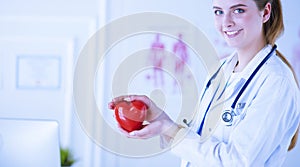 Female doctor with stethoscope holding heart, on light background