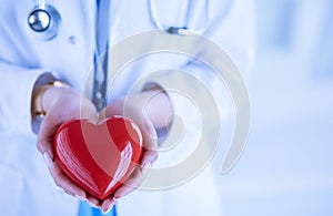 Female doctor with stethoscope holding heart, on light background