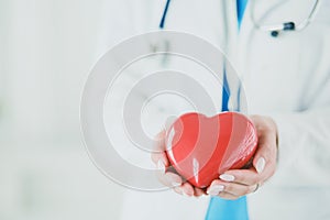 Female doctor with stethoscope holding heart, on light background