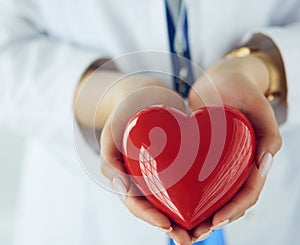 Female doctor with stethoscope holding heart, on light background