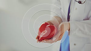 Female doctor with stethoscope holding heart, on light background