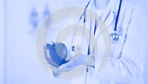 Female doctor with stethoscope holding heart, on light background